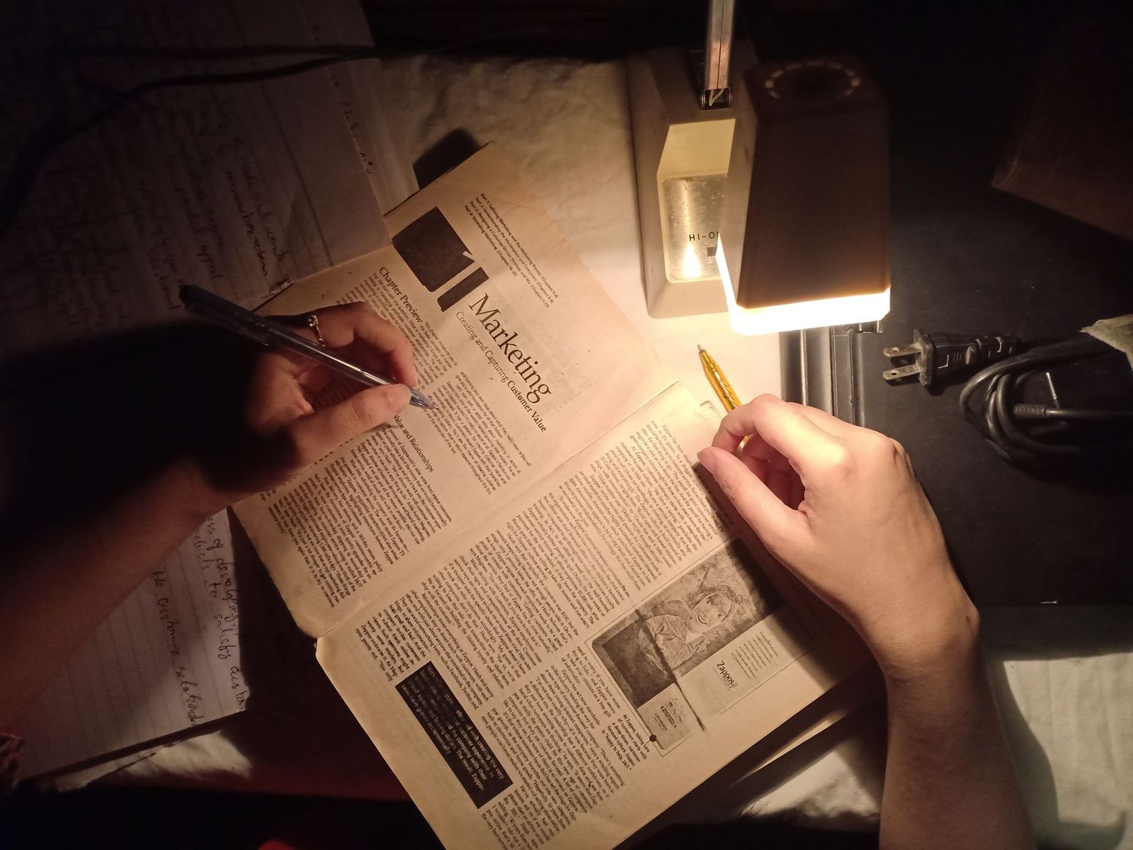 a woman’s hand holding a pen over a torn notebook page on a nightstand under lamp light. || woman’s hand holding pen over torn notebook page nightstand under lamp light thirties