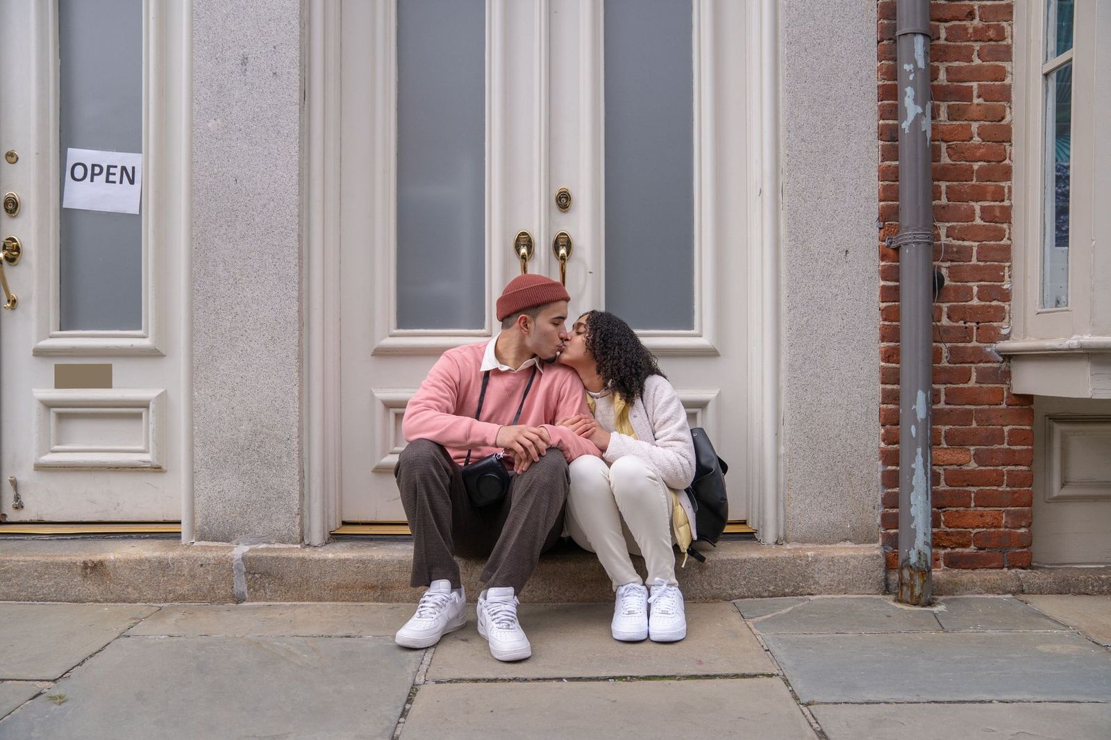 couple their thirties sitting close porch step one holds half full wine bottle they are talking not kissing body language open but little awkward