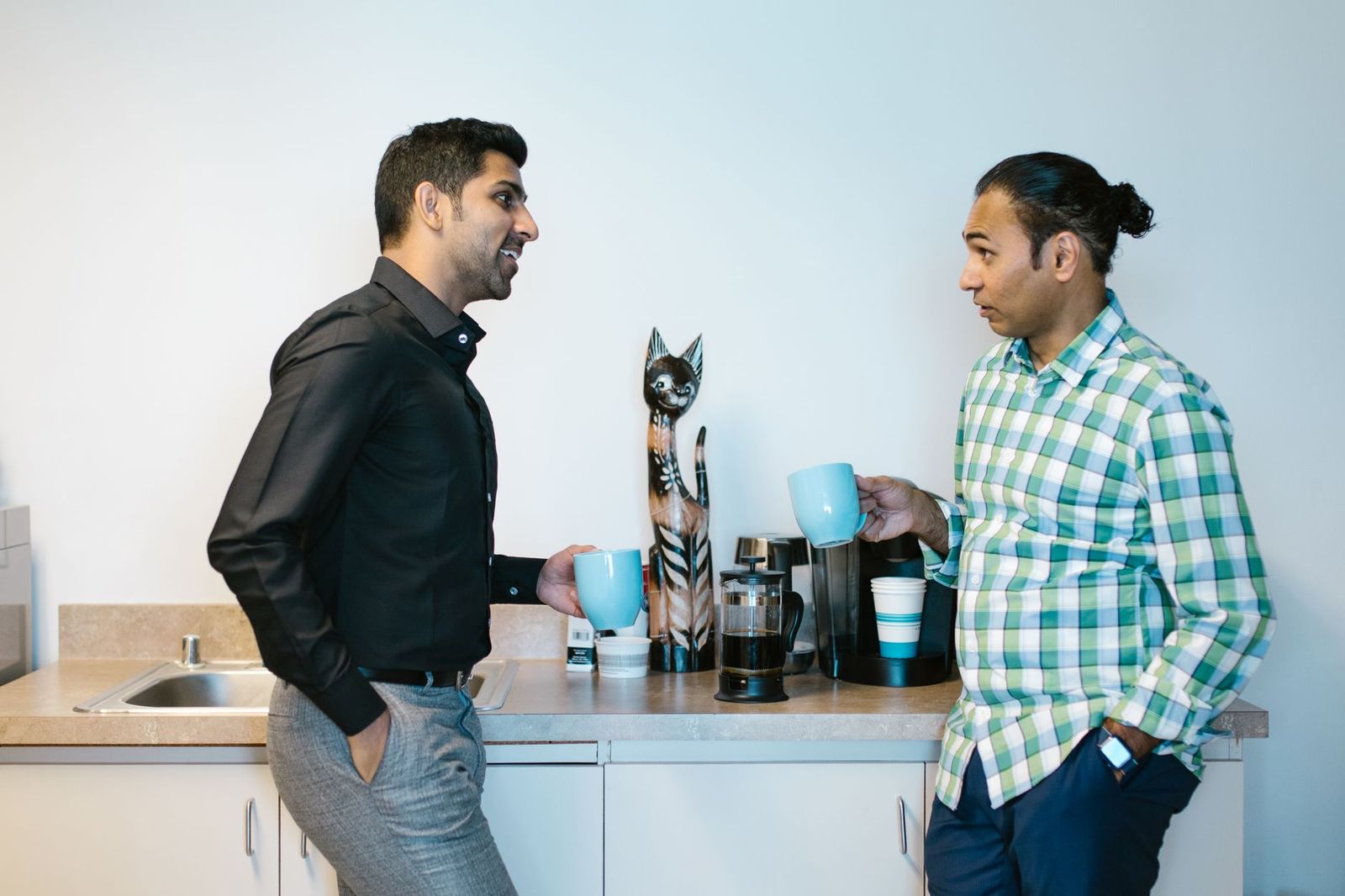 two colleagues their mid thirties standing step too close office kitchen counter after hours one holding mug fluorescent light the moment before question asked