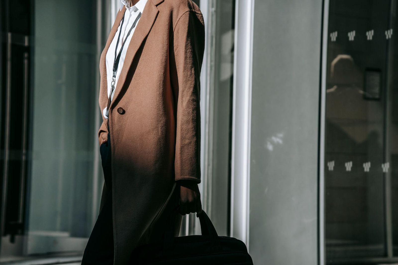 a woman in her thirties walking out of an office building in daylight, coat on, looking forward || woman her thirties walking out office building coat looking forward