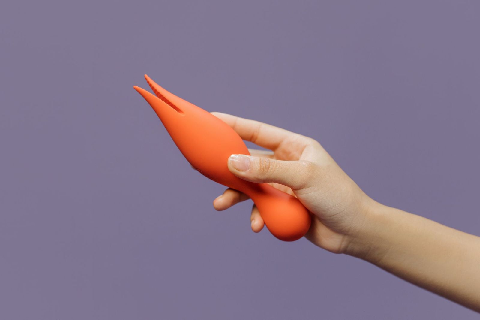 A hand holding a silicone vibrator against a minimal backdrop