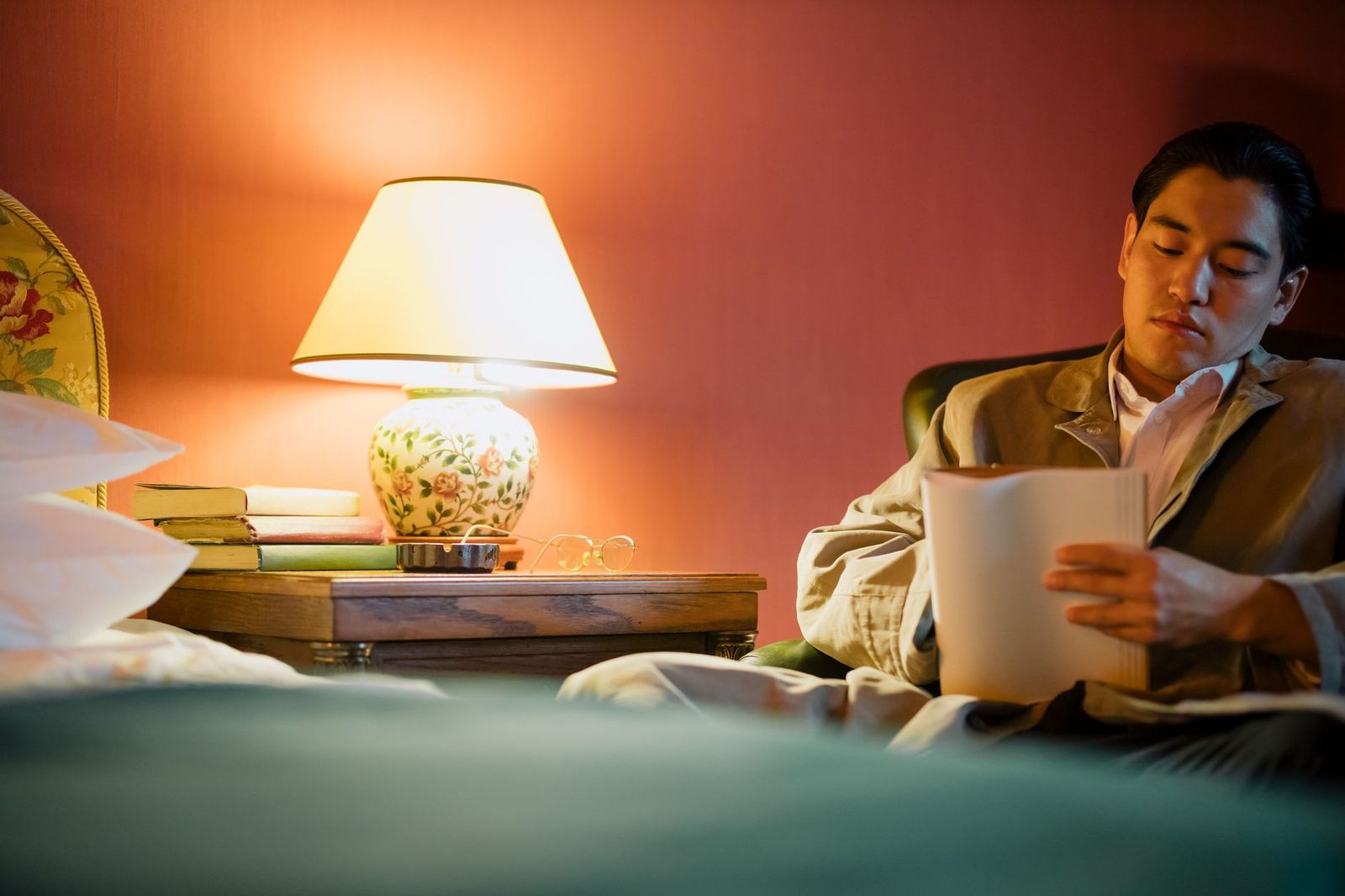 woman her thirties sitting bed duvet bunched around her waist bedside lamp one hand pressed her own collarbone man's arm the frame's edge