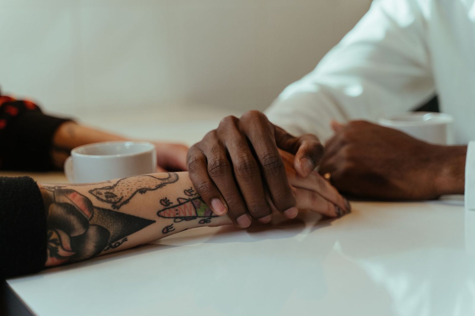 two coffee cups on a table between two people mid-conversation, hands visible, faces not required || two coffee cups table between two people mid conversation hands visible faces not required thirties