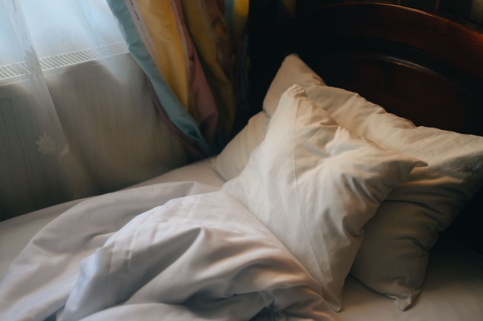 an unmade bed in morning light, one pillow clearly last slept on and the other untouched, no people. || unmade bed light one pillow clearly last slept and the other untouched people thirties