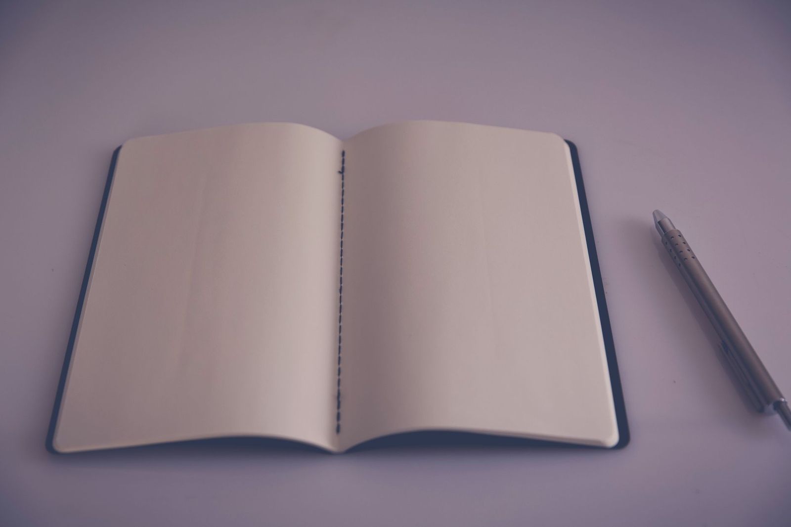 a small notebook and a pen on a nightstand next to a lamp, one page open. || notebook and pen nightstand next lamp one page open