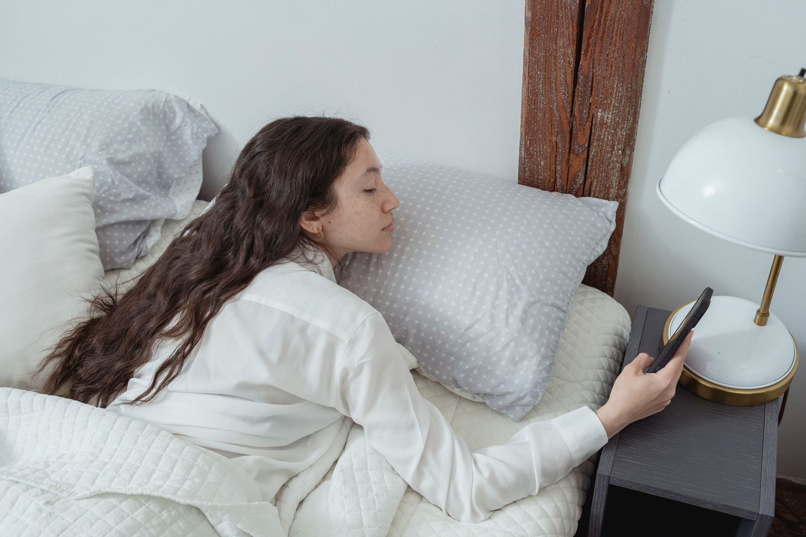 woman her mid thirties lying bed one hand resting heating pad over her lower belly phone face down the sheet beside her and awake not posed