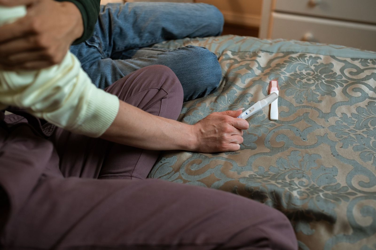 a nightstand at night holding a hot water bottle, a phone showing a period tracker screen, and a pregnancy test box — readable domestic objects, no people || nightstand holding hot water bottle phone showing period tracker screen and pregnancy test box readable domestic objects people thirties