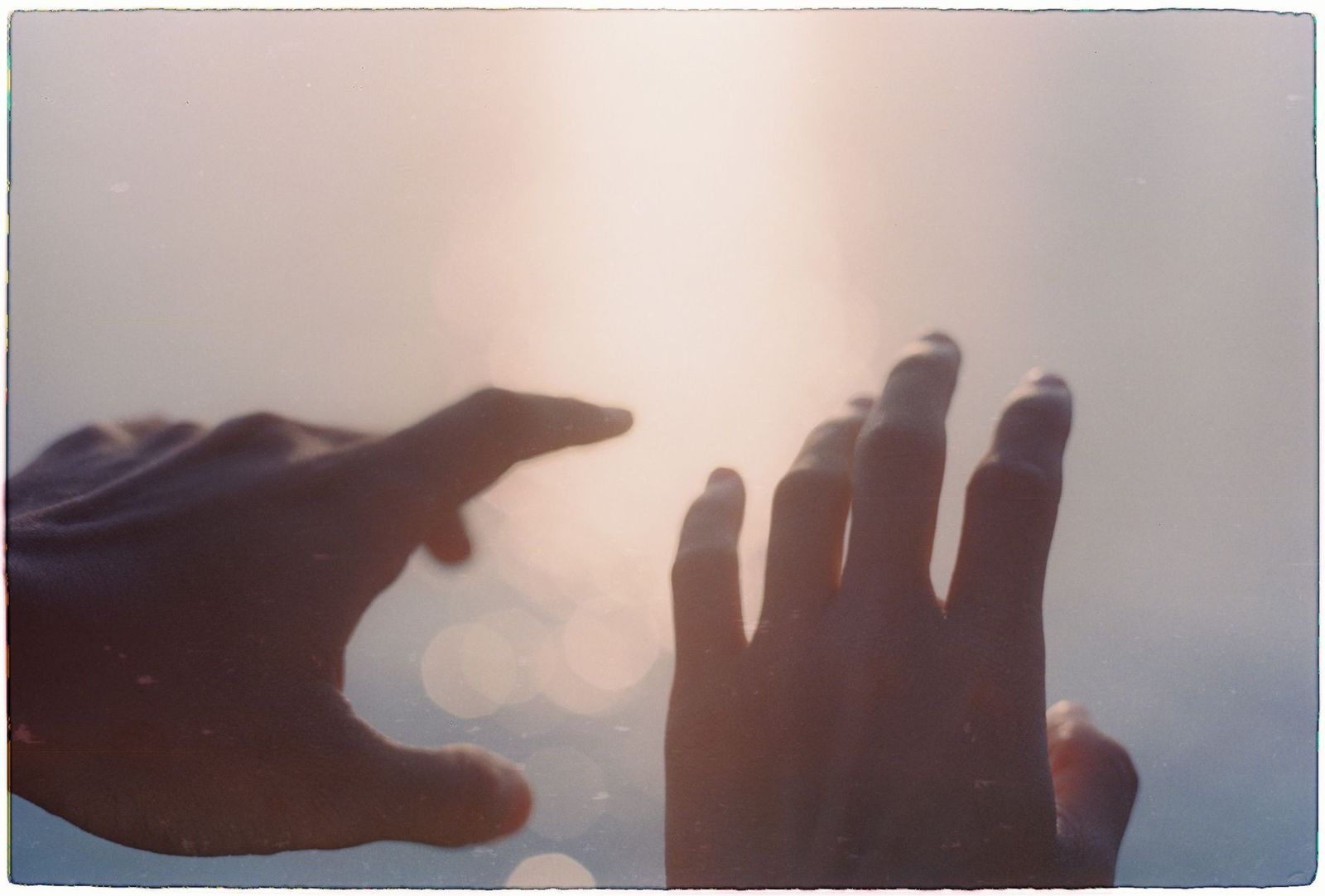 a hand reaching toward another pair of hands on a duvet in low morning light || hand reaching toward another pair hands duvet low light