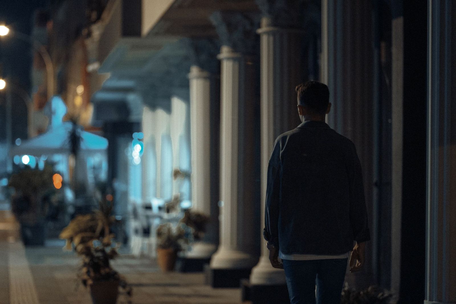 a woman walking alone at night on a city sidewalk, holding shoes, looking determined. || woman walking alone city sidewalk holding shoes looking determined thirties