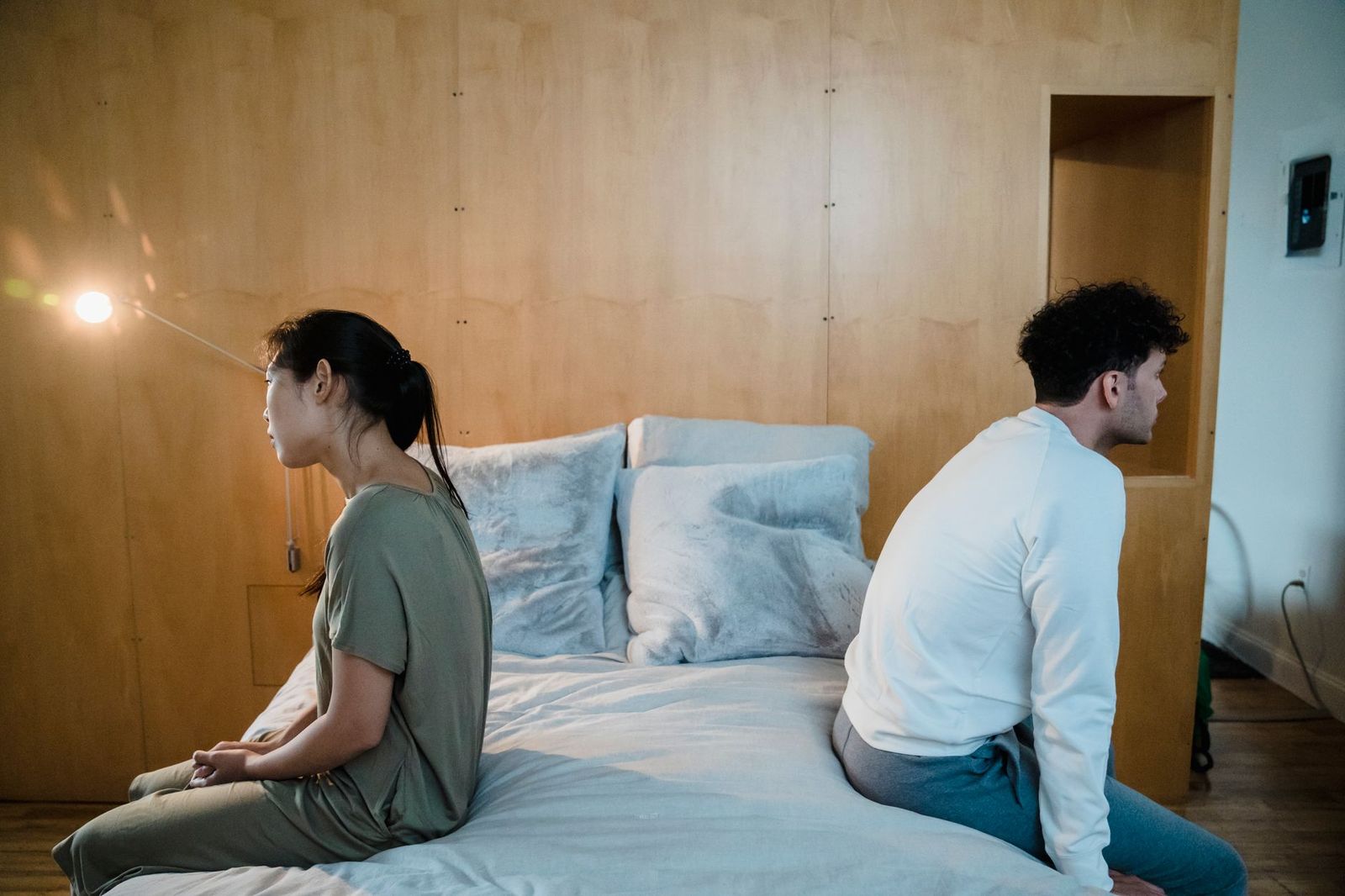 couple their late thirties bedroom lies his back with eyes closed she sits watching his face low lamp light
