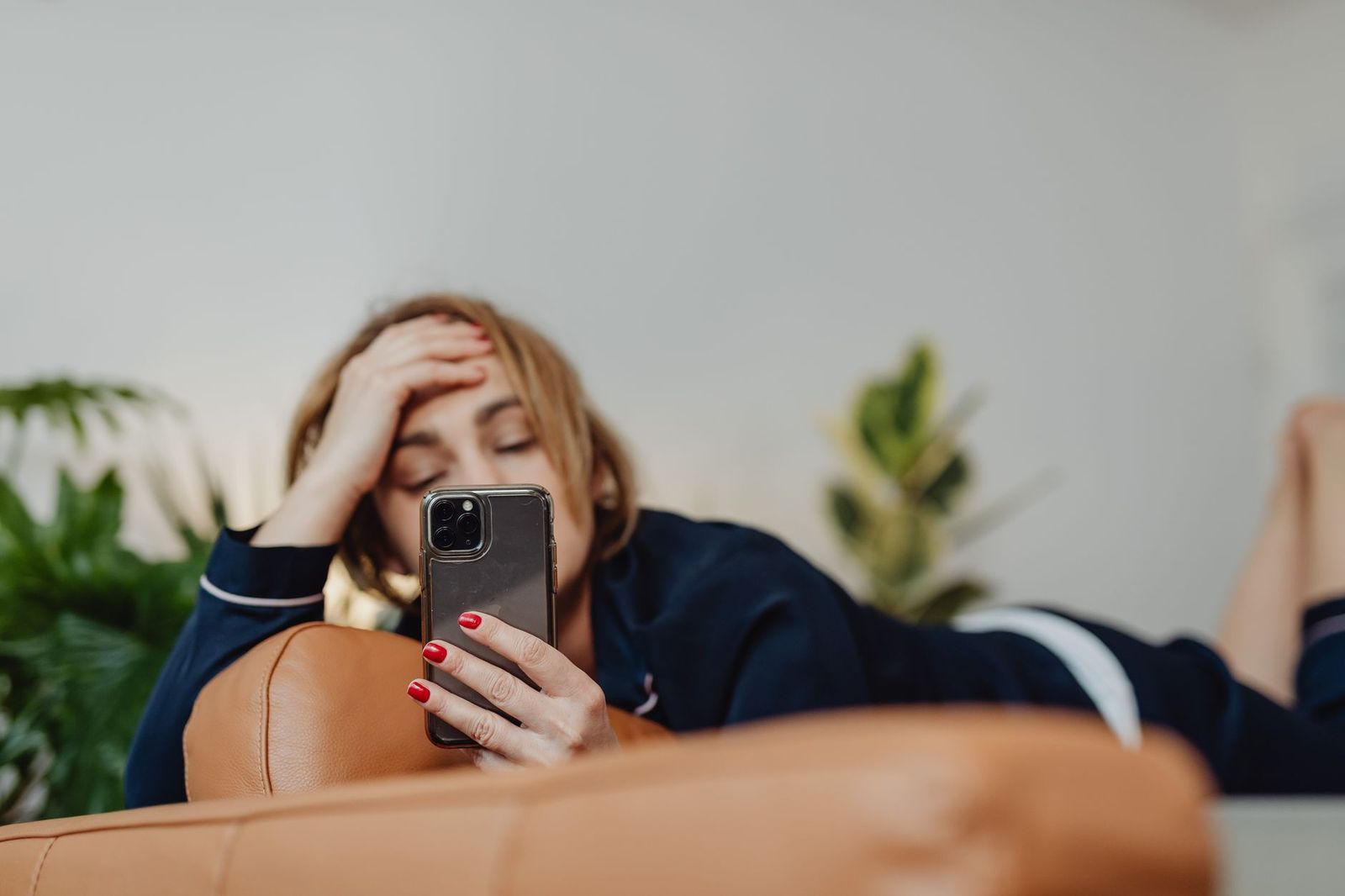 a woman in her thirties in pajamas on a sofa at night, holding her phone, her face lit, thinking || woman her thirties pajamas sofa holding her phone her face lit thinking