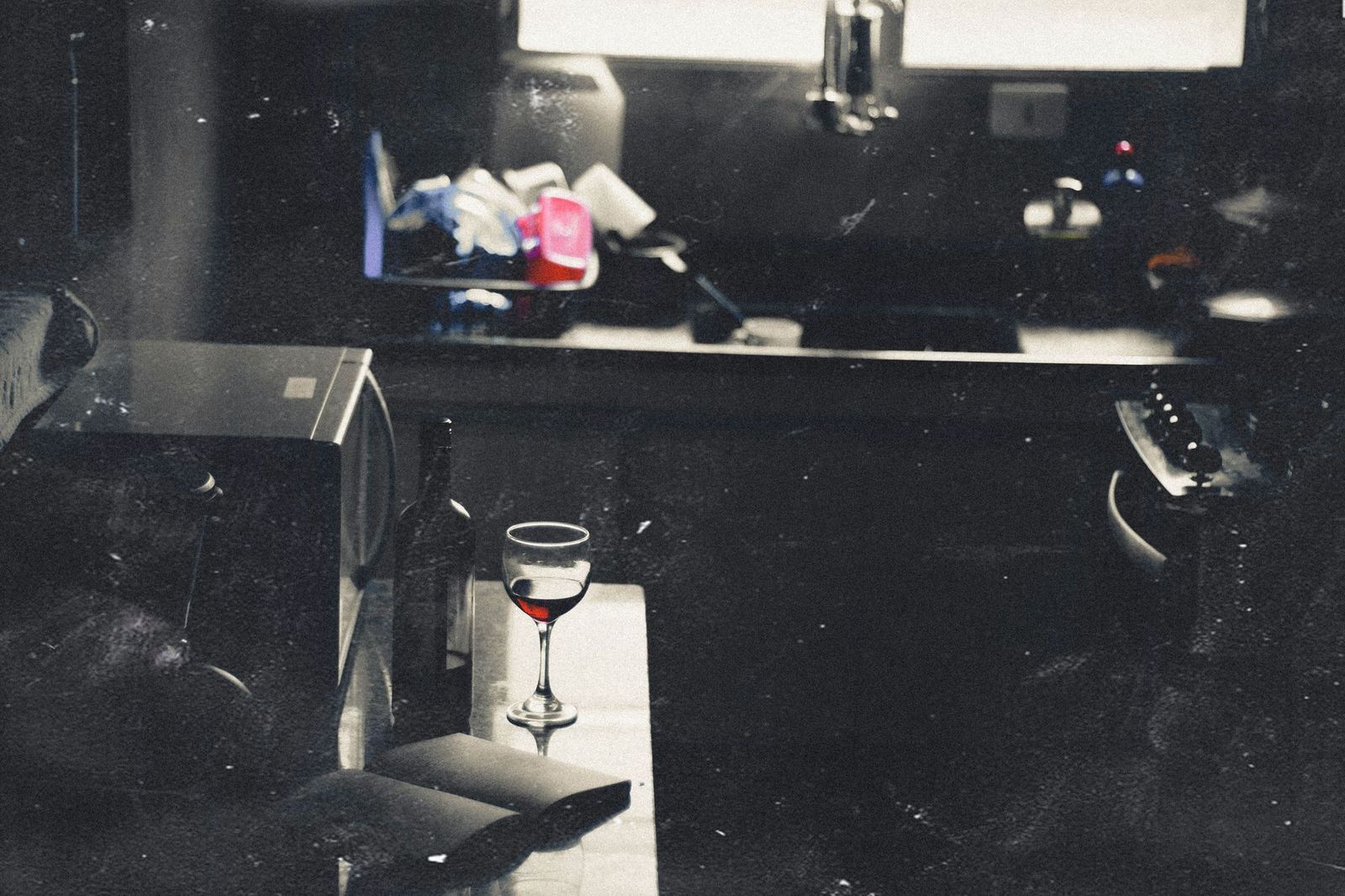 woman her mid thirties kitchen table phone one hand half glass wine stack kids' school papers light